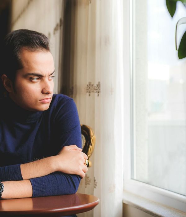 Person looking thoughtfully out a window with a green plant nearby.